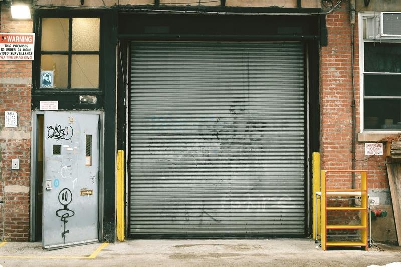 A closed roll-up door beside a sign warning the premises is under 24-hour video surveillance