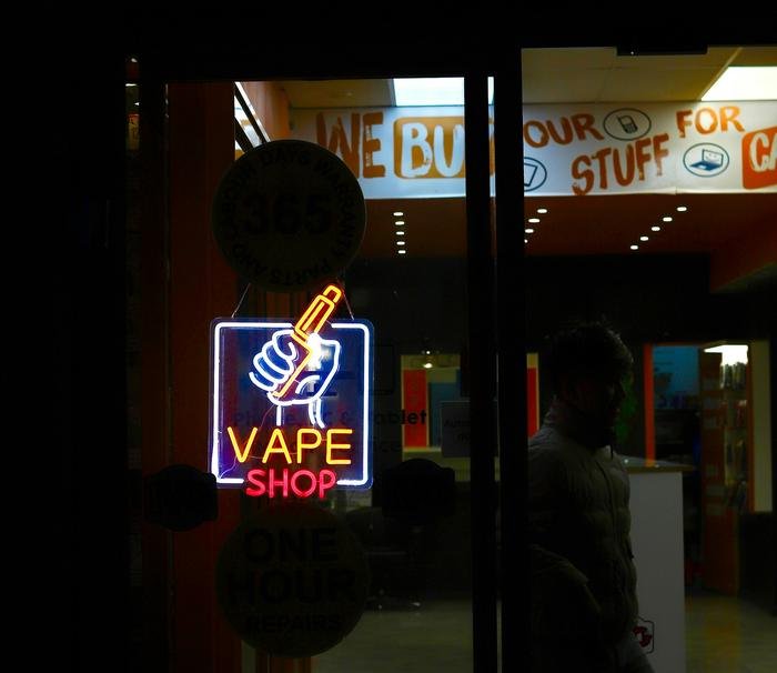 A neon vape shop sign in a dark doorway